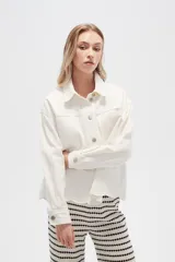 Campera de jean color crudo, de corte recto, con cuello clásico, cierre frontal con botones metálicos, dos bolsillos con solapa en el pecho y bajo con detalle de bordado calado.