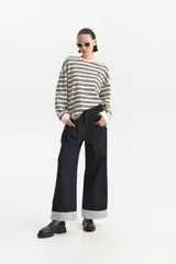 Jean ancho de tiro medio en denim oscuro, con bajos doblados que revelan un forro interior a rayas blancas y negras.