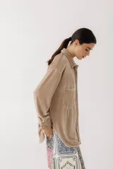 Camisa beige de terciopelo con cuello clásico, cierre frontal con botones, dos bolsillos de parche en el pecho y mangas largas con puños abotonados.