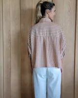 Camisa color beige con rayas verticales blancas, cuello clásico, mangas 3/4 y bolsillos frontales cuadrados.