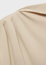 Camiseta color beige de tejido fluido con cuello asimétrico, diseño recto y detalles fruncidos.