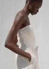 Mono largo color crudo, sin mangas, con cuello escotado, trabillas, cinturón desmontable y bolsillos laterales con cierre de cremallera.