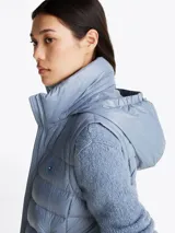 Chaleco acolchado celeste con cuello alto, cierre frontal con cremallera, dos bolsillos laterales con cremallera y logo de la marca en el pecho. Tiene mangas de tejido de punto. Repele el agua y tiene relleno de plumón.