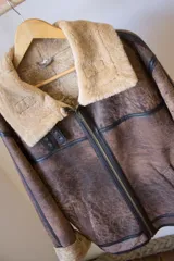 Campera gamulán marrón con cuello y puños de piel sintética color beige. Cierre frontal con cremallera y bolsillos laterales.