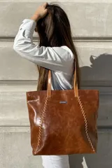 Bolso grande tipo tote de cuero color marrón con costuras decorativas en los laterales, forro interior con bolsillo para celular y bolsillo con cierre. Incluye bolsillo trasero con cierre y correas largas para colgar del hombro.
