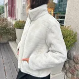 Campera de cuero ovino color tostado con interior de piel sintética blanca. Tiene cuello alto con solapas y cierre frontal con cremallera.