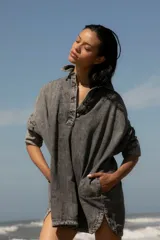 Vestido camisero de denim gris con cuello camisero, cierre frontal con botones, mangas largas con puños abotonados, bolsillos laterales y apliques bordados en el pecho y la manga. Corte holgado y largo a la rodilla.