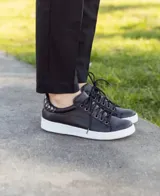 Zapatillas acordonadas de cuero color marrón con detalles dorados en el talón y suela blanca.