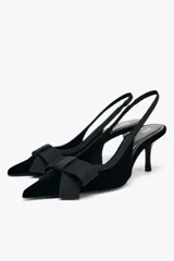 Zapato destalonado negro de terciopelo con tacón fino y tira trasera elástica. Detalle de lazo en la parte delantera.