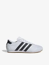 Zapatillas Adidas de cuero blanco con las tres tiras laterales en negro y suela de goma color caramelo.