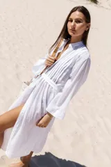 Camisola larga tipo túnica de voile de algodón color blanco, con cuello mao, tablitas a los costados desde el hombro hasta el pecho, manga amplia estilo kimono, lazos a los costados a la altura de la cintura, tajos a los costados y cierre con botones de pasta aplicados en tríos.
