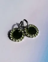 Aros colgantes con forma circular, hechos de resina color lila y borde de strass plateado. El aro es de acero quirúrgico plateado.