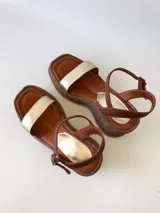 Sandalias de cuero con plataforma, color marrón con tira dorada sobre los dedos y tobillera marrón con hebilla.