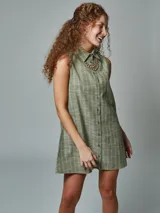Vestido corto sin mangas color verde oliva con rayas blancas, cuello camisero y cierre frontal con botones. Incluye collar dorado de eslabones gruesos.