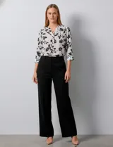 Blusa de gasa blanca con estampado floral en negro. Presenta cuello a la base con escote en V y abertura con botones. Las mangas son largas y se pueden ajustar a tres cuartos.