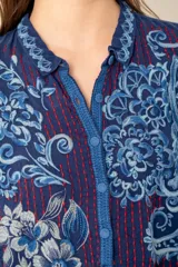 Túnica azul con bordados florales, cuello camisero y botones forrados.