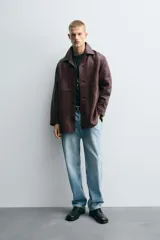 Cazadora de hombre de corte relajado, confeccionada en piel con textura irregular color marrón oscuro (vino/borgoña). Presenta cuello solapa, manga larga con puño abotonado, bolsillos de vivo en cadera, bolsillo interior y cierre frontal con botonadura.