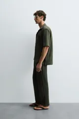 Camisa verde militar de corte relaxed fit, con cuello bowling, manga corta, bajo con aberturas laterales y cierre frontal de botonadura.