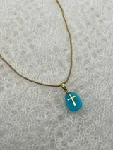 Collar con cadena dorada y dije de piedra natural celeste con cruz dorada.