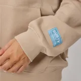 Canguro beige con capucha, cordones ajustables, bolsillo tipo canguro y puños y ruedo acanalados. Estampado frontal con el logo de la marca y la frase "Australian Surf Girl".