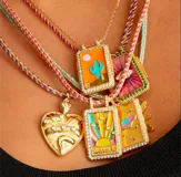 Collar dorado con dijes rectangulares con diseños esmaltados de sol, cactus y planeta, y dije de corazón con strass.