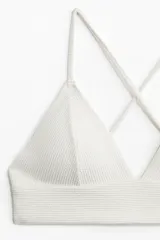 Top de bikini blanco con copas de triángulo con relleno extraíble, breteles finos ajustables y tiras cruzadas en la espalda. Sin aros ni cierre. Forrado.