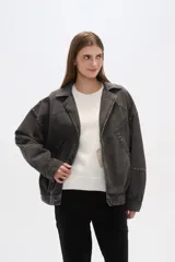 Campera de jean celeste con cuello clásico, solapas, cierre frontal con botones metálicos y mangas largas con puños abotonados. Presenta detalles de costuras diagonales y apliques de tachas metálicas.