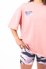 Remera oversize rosa con estampado en la espalda que incluye texto y una ilustración de dos personas cayendo.