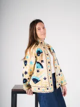 Chaqueta color crema con bordados de flores y figuras geométricas en tonos azul, celeste y dorado.