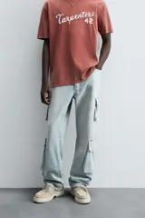 Pantalón de denim color beige, corte relaxed fit, con bolsillos laterales tipo cargo con solapa y cierre de botón. Cierre frontal con botón y cremallera.