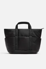 Bolso tipo shopper negro fabricado en tejido técnico. Cuenta con un compartimento principal con cierre de cremallera y un bolsillo interior con cierre. En la parte frontal tiene tres bolsillos. Tiene dos asas de mano.