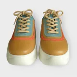Zapatillas urbanas color mostaza, con detalles en verde menta y naranja. Confeccionadas en cuero sintético con cordones beige y suela de plataforma blanca.