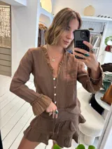 Blusa color beige de lino, con escote en V adornado con volados y botones de nácar. Las mangas largas terminan en puños con volados.