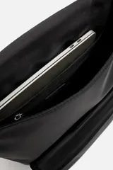 Mochila negra de tejido técnico con solapa y hebilla. Tiene un bolsillo frontal, un bolsillo interior con cierre y un compartimento para dispositivos electrónicos de hasta 13 pulgadas. La parte posterior es acolchada y tiene una banda de sujeción para equipaje.