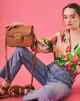 Bandolera color beige con textura símil reptil, cierre con broche metálico dorado y correa larga regulable.