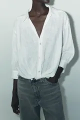Camisa blanca de cuello solapa y manga larga con puños. Tiene un nudo en la parte delantera y cierre frontal con botones.
