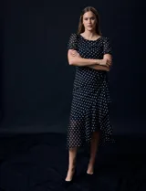 Vestido midi de gasa color negro con lunares blancos, con mangas cortas, escote redondo y ruedo asimétrico. Presenta un frunce lateral con lazo de ajuste.