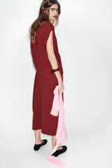 Vestido largo color borgoña, con escote barco y manga caída/sisa. Presenta un drapeado lateral que genera un bajo asimétrico.