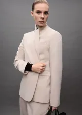 Chaqueta color beige con cuello de pico con solapa, hombros estructurados, cierre delantero con botón, dos bolsillos de ribete en la parte delantera y un bolsillo de ribete en el pecho.