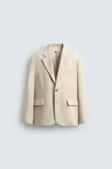 Blazer color beige confeccionado en tejido con lana, de corte relajado. Tiene cuello con solapas de muesca, manga larga con puños abotonados, bolsillo de vivo en el pecho, bolsillos de solapa en la cadera, bolsillo interior, bajo con abertura en el centro de la espalda y cierre frontal con botones.