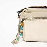Bandolera beige de tela con correa marrón y dije de cuentas de colores.