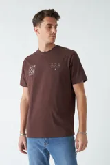 Remera marrón de algodón con cuello redondo, corte regular y estampado en el pecho. El modelo usa talle M.