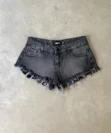 Short de jean negro con efecto acid wash, tiro bajo, con roturas y terminación deshilachada en el ruedo. Presenta detalles de ojales metálicos y tiras de ajuste laterales.