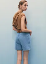 Short pantalón (skort) de denim azul claro, tiro medio, con diseño cruzado en la parte delantera asegurado con un botón y cierre de cremallera en la parte posterior.