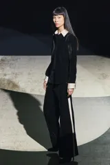 Camisa negra de terciopelo con cuello solapa, manga larga con puños en tejido color crema a contraste y bajo redondeado.