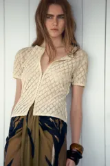 Top color crema de tejido de punto calado con patrón de rombos, cuello redondo, manga corta y cierre frontal con ganchos metálicos.