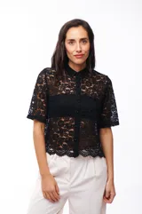 Camisa blanca de encaje con cuello clásico, cierre frontal con botones y mangas cortas.