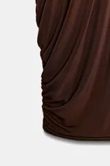 Vestido corto marrón con cuello halter y hombros descubiertos. Tiene detalle de tejido drapeado en los laterales y bajo abullonado con elástico. El forro interior está combinado con aplicación de lentejuelas.