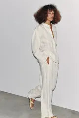 Pantalón blanco de lino con tiro medio, cintura ajustable con cordones, bolsillos laterales ocultos y detalle de entredós combinados a tono.