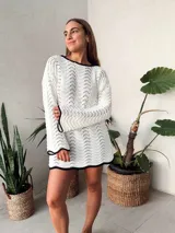 Vestido corto tejido al crochet color blanco, con mangas largas y escote redondo con borde negro.